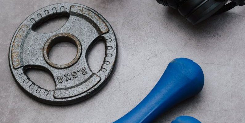 Blue Hole - From above of dumbbells with plate and fitness bottle near contemporary wireless headphones on gray background