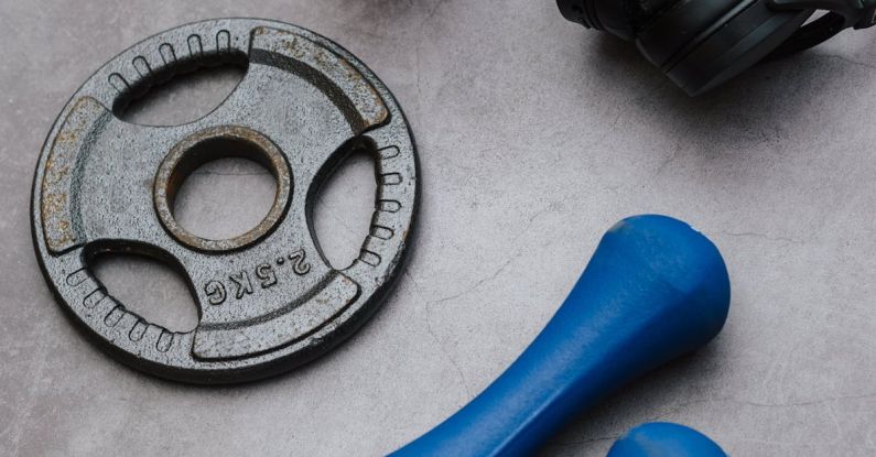 Blue Hole - From above of dumbbells with plate and fitness bottle near contemporary wireless headphones on gray background