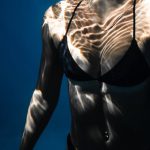 Dive Checklist - Underwater shot of fit young female in black bikini swimming in dark blue seawater with eyes closed