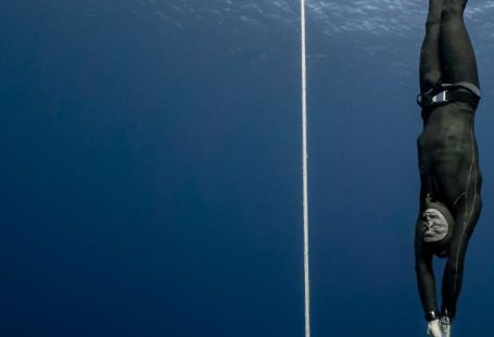 Conservation Diving - Full body of sporty male swimmer in black swimsuit diving in deep turquoise water of magnificent ocean