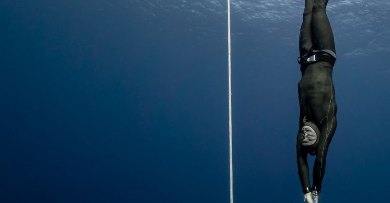 Conservation Diving - Full body of sporty male swimmer in black swimsuit diving in deep turquoise water of magnificent ocean