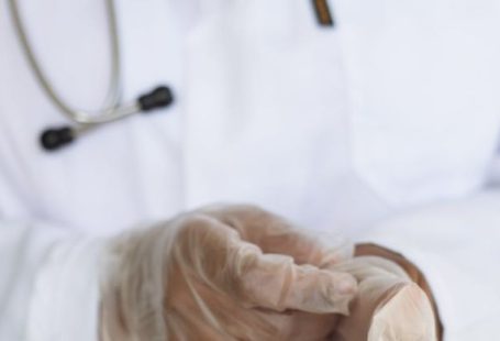Medical Checks - Faceless ethnic medical worker in lab coat and stethoscope taking of transparent gloves after approaching patients for examination in modern hospital