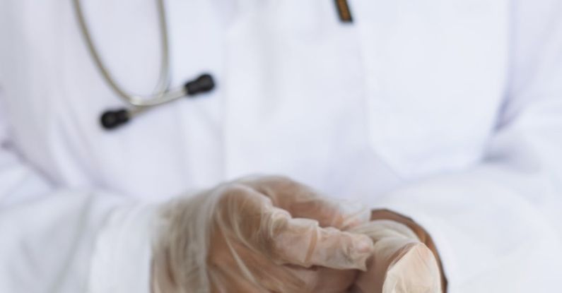 Medical Checks - Faceless ethnic medical worker in lab coat and stethoscope taking of transparent gloves after approaching patients for examination in modern hospital