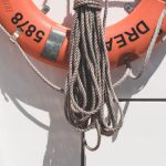 Marine Protected - Orange lifebuoy with tied mooring rope hanging on white wall of modern yacht on sunny day