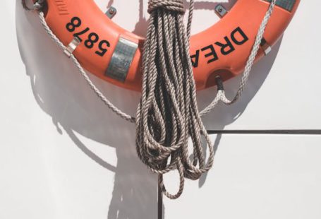 Marine Protected - Orange lifebuoy with tied mooring rope hanging on white wall of modern yacht on sunny day