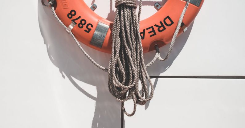 Marine Protected - Orange lifebuoy with tied mooring rope hanging on white wall of modern yacht on sunny day